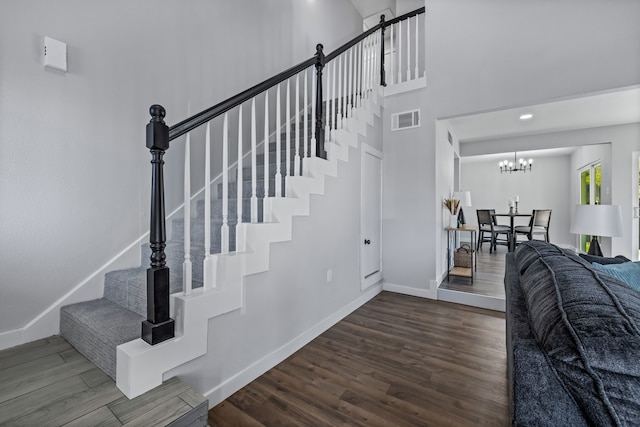 stairway featuring a notable chandelier, hardwood / wood-style flooring, and a high ceiling