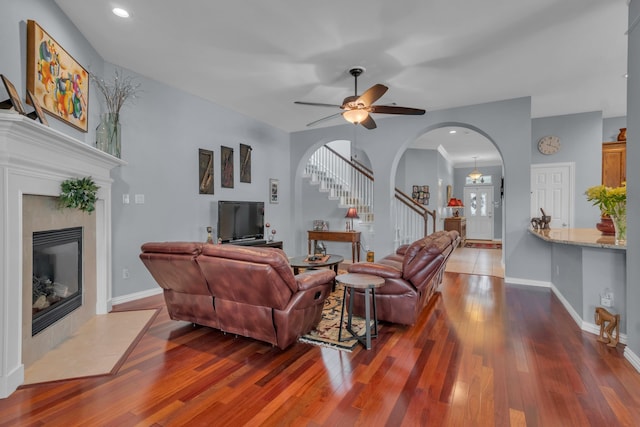 living room with a tiled fireplace, wood-type flooring, and ceiling fan