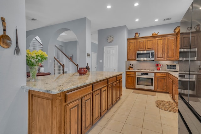 kitchen featuring decorative backsplash, a kitchen island, light tile patterned floors, appliances with stainless steel finishes, and light stone counters