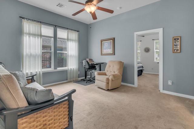 living area with ceiling fan, plenty of natural light, and light colored carpet