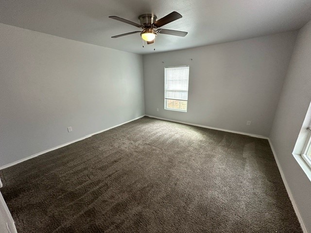 empty room featuring ceiling fan and dark carpet