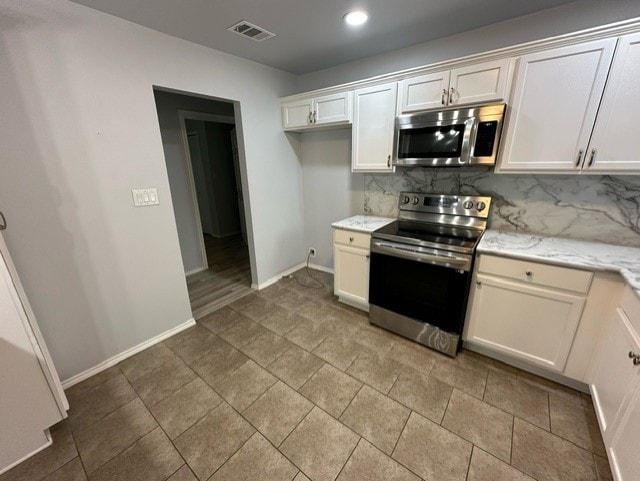 kitchen featuring white cabinets, light stone counters, stainless steel appliances, and backsplash