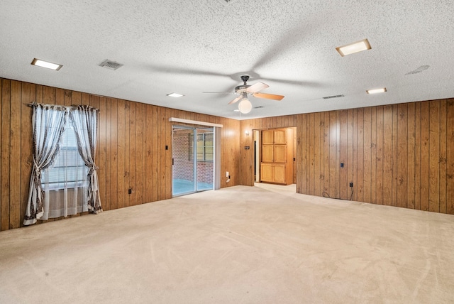 carpeted empty room with a healthy amount of sunlight, wooden walls, and ceiling fan