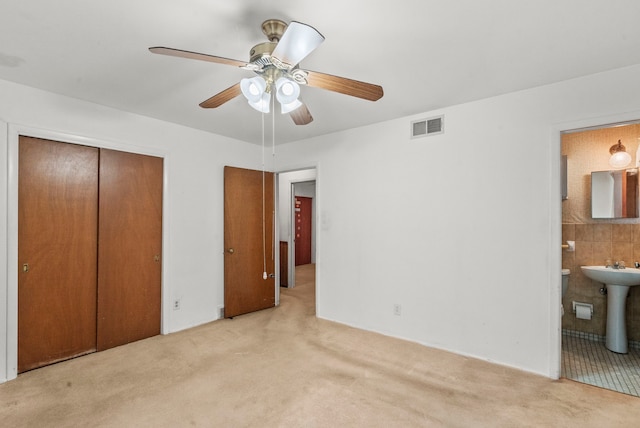 unfurnished bedroom with light carpet, a closet, ensuite bathroom, and ceiling fan