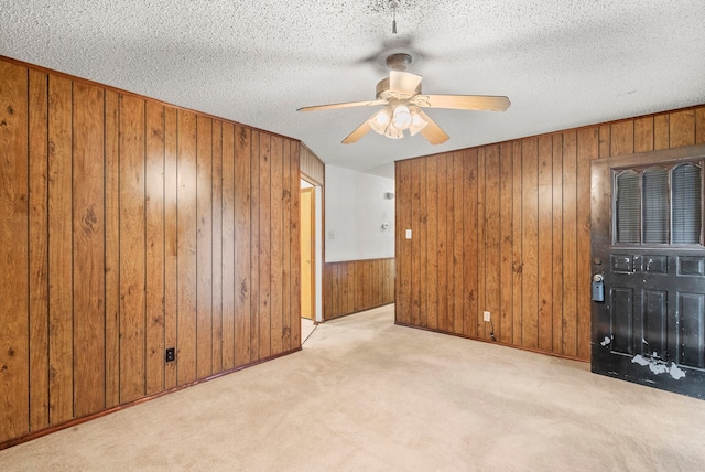 spare room featuring light carpet, a textured ceiling, wooden walls, and ceiling fan