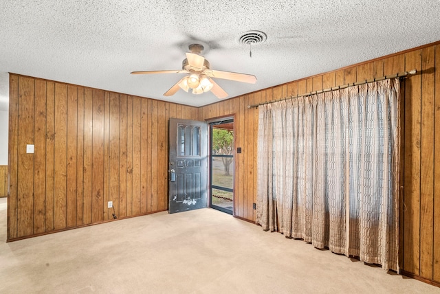 carpeted spare room featuring wooden walls, a textured ceiling, and ceiling fan