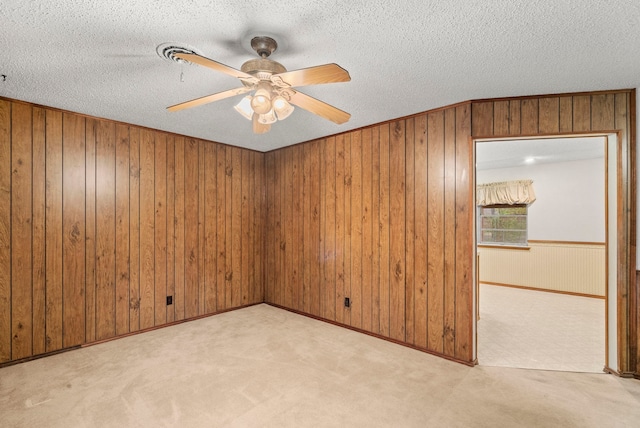 carpeted empty room featuring ceiling fan, a textured ceiling, and wood walls