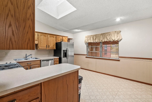 kitchen with vaulted ceiling with skylight, a textured ceiling, appliances with stainless steel finishes, and sink