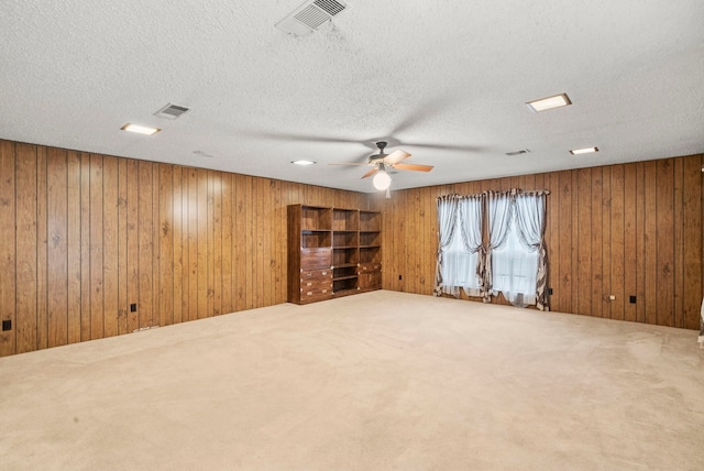 carpeted spare room featuring ceiling fan, wood walls, and a textured ceiling