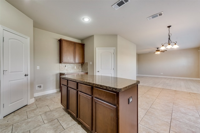 kitchen featuring a kitchen island, pendant lighting, light tile patterned floors, ceiling fan with notable chandelier, and tasteful backsplash