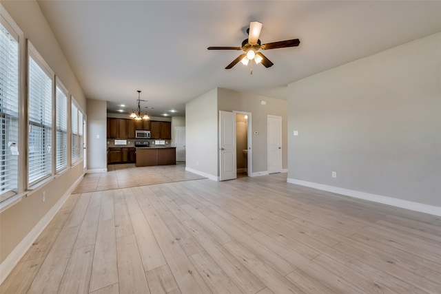 unfurnished living room with ceiling fan with notable chandelier and light hardwood / wood-style floors