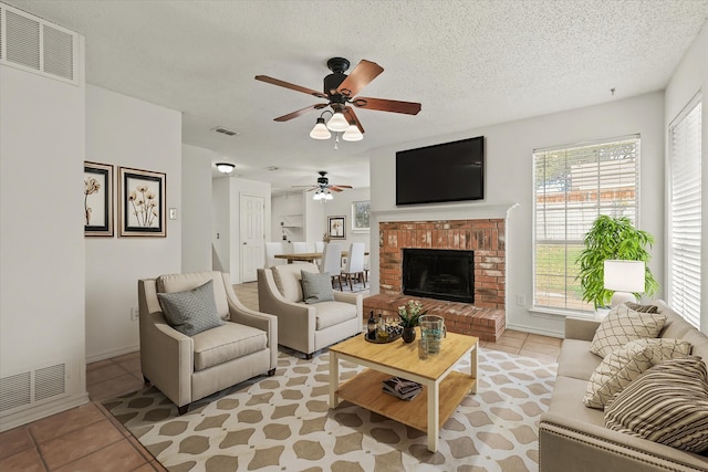 living room featuring a textured ceiling, ceiling fan, light tile patterned flooring, and a brick fireplace