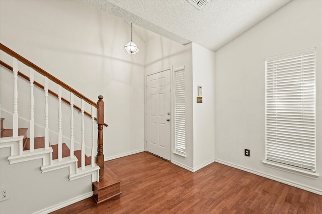 entrance foyer featuring vaulted ceiling, wood-type flooring, and a textured ceiling