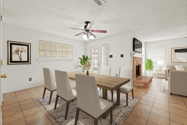 dining area featuring a textured ceiling, ceiling fan, a fireplace, and light tile patterned floors