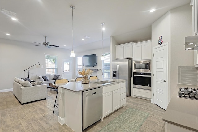 kitchen with sink, hanging light fixtures, stainless steel appliances, a center island with sink, and white cabinets