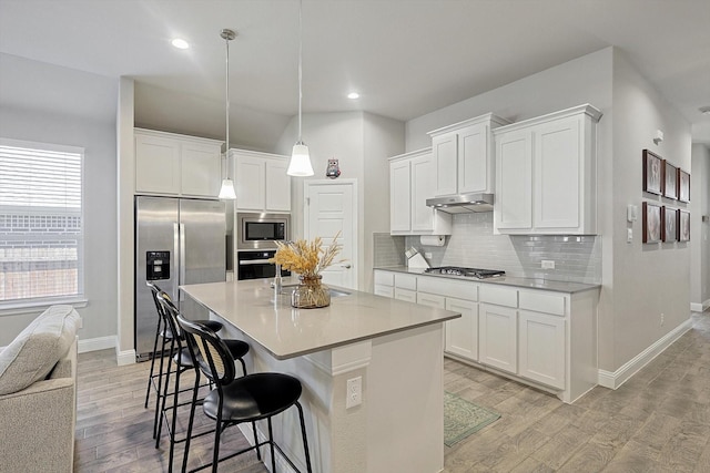 kitchen featuring white cabinetry, hanging light fixtures, stainless steel appliances, a breakfast bar, and a center island with sink