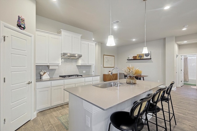 kitchen featuring light wood-type flooring, sink, decorative light fixtures, a center island with sink, and white cabinets