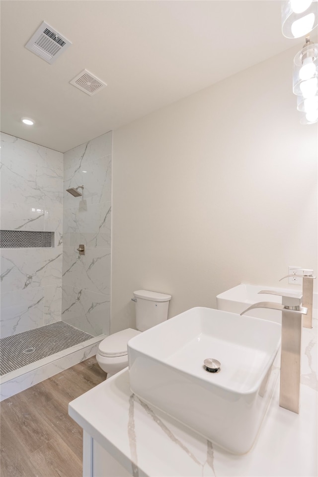 bathroom featuring wood-type flooring, vanity, toilet, and a tile shower