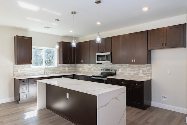 kitchen featuring stainless steel appliances, light wood-type flooring, pendant lighting, light stone countertops, and a center island