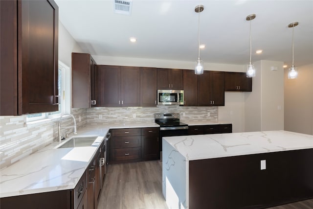 kitchen with light stone counters, sink, a kitchen island, appliances with stainless steel finishes, and decorative light fixtures