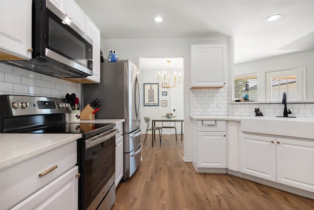 kitchen with sink, backsplash, appliances with stainless steel finishes, white cabinets, and light wood-type flooring