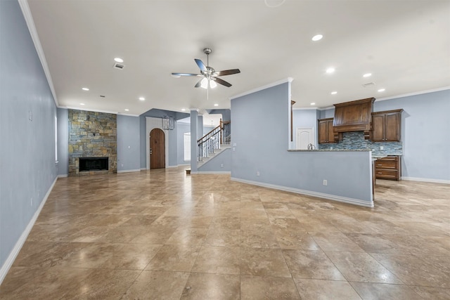 unfurnished living room with a stone fireplace, ceiling fan, ornamental molding, and sink