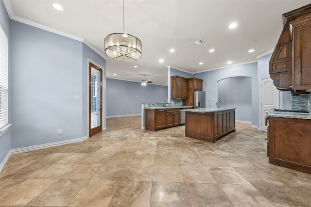 kitchen featuring light stone countertops, ceiling fan with notable chandelier, stainless steel appliances, a kitchen island with sink, and decorative light fixtures