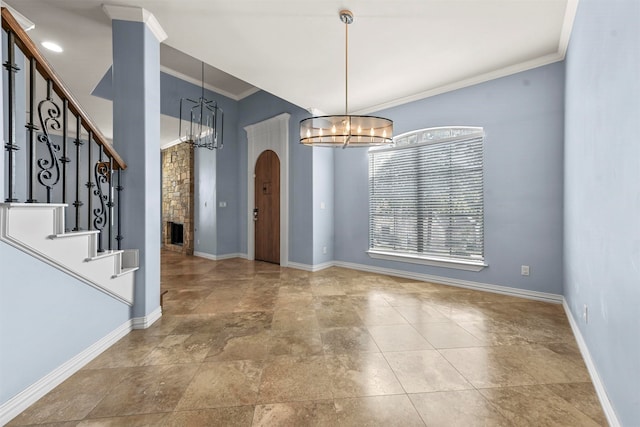 foyer entrance with a stone fireplace, crown molding, and a notable chandelier