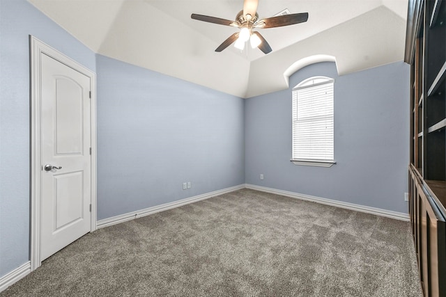 empty room with dark colored carpet, ceiling fan, lofted ceiling, and a tray ceiling