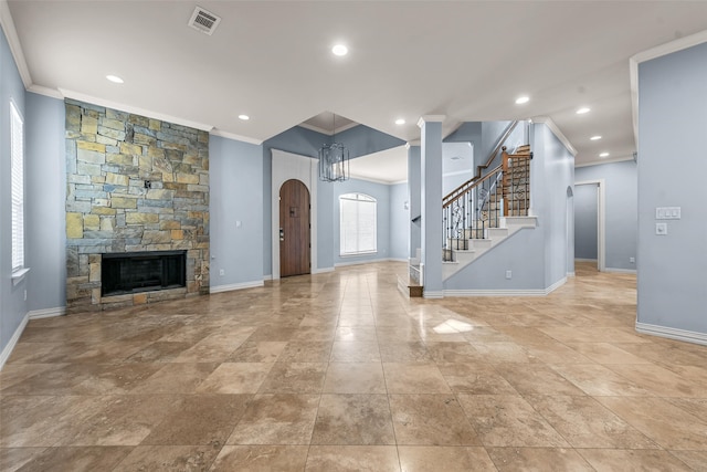 unfurnished living room featuring a stone fireplace, crown molding, and a chandelier