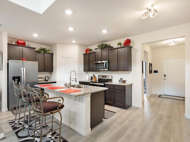 kitchen with sink, a kitchen breakfast bar, light hardwood / wood-style flooring, an island with sink, and appliances with stainless steel finishes