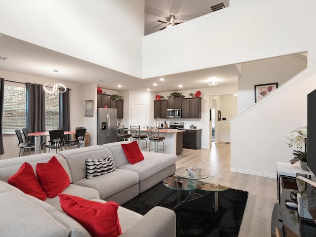 living room with ceiling fan, a towering ceiling, sink, and light hardwood / wood-style flooring