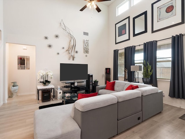 living room with ceiling fan, a high ceiling, and light wood-type flooring