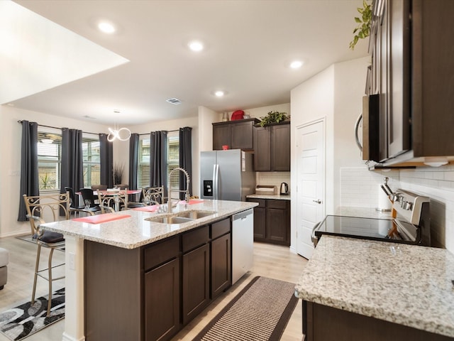 kitchen with sink, stainless steel appliances, light stone counters, light hardwood / wood-style floors, and a kitchen island with sink