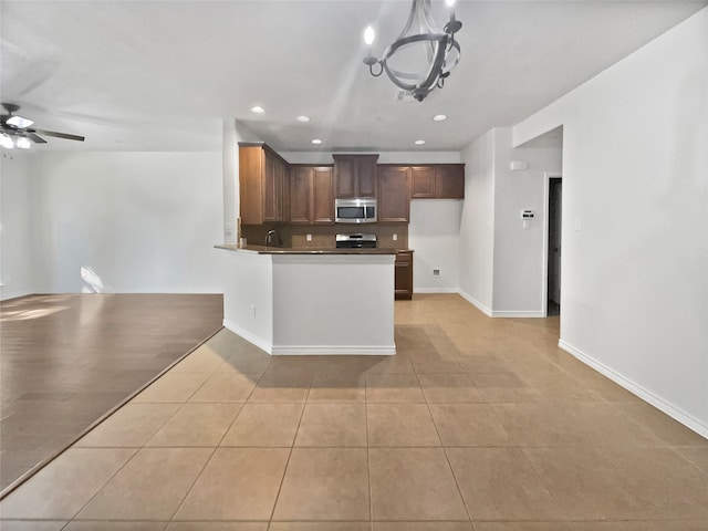 kitchen featuring appliances with stainless steel finishes, kitchen peninsula, light tile patterned flooring, and ceiling fan with notable chandelier