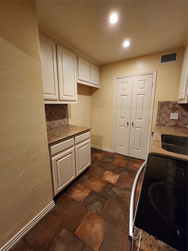 kitchen featuring tasteful backsplash, sink, white cabinets, and range