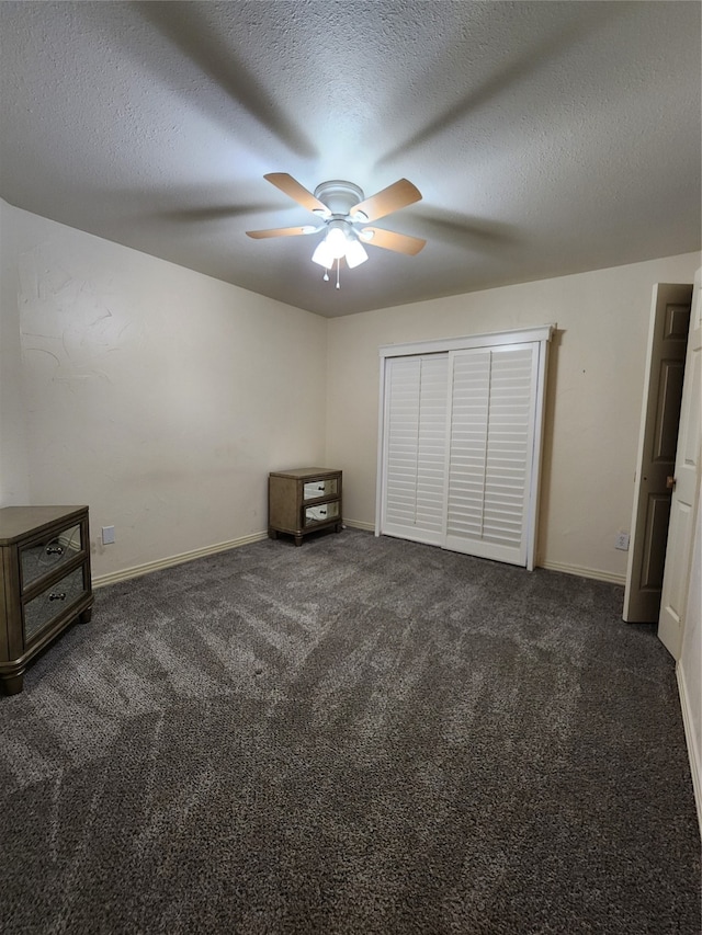 unfurnished bedroom with dark colored carpet, a textured ceiling, a closet, and ceiling fan