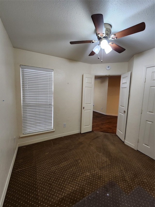 unfurnished room with dark colored carpet, ceiling fan, and a textured ceiling