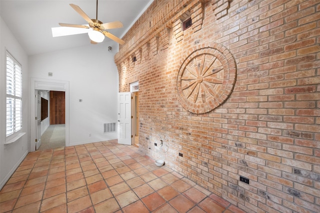 unfurnished living room with ceiling fan, brick wall, and vaulted ceiling with skylight