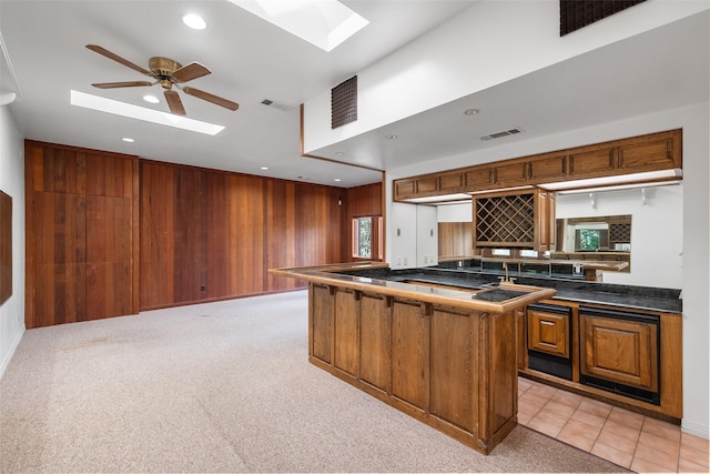 kitchen with light carpet, a skylight, kitchen peninsula, wooden walls, and ceiling fan