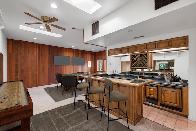 kitchen with a skylight, kitchen peninsula, a breakfast bar area, ceiling fan, and tile patterned floors