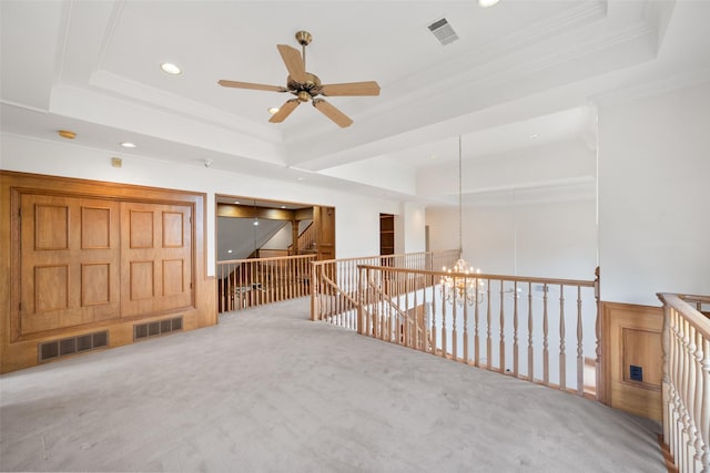 carpeted empty room with ceiling fan with notable chandelier, a tray ceiling, and ornamental molding