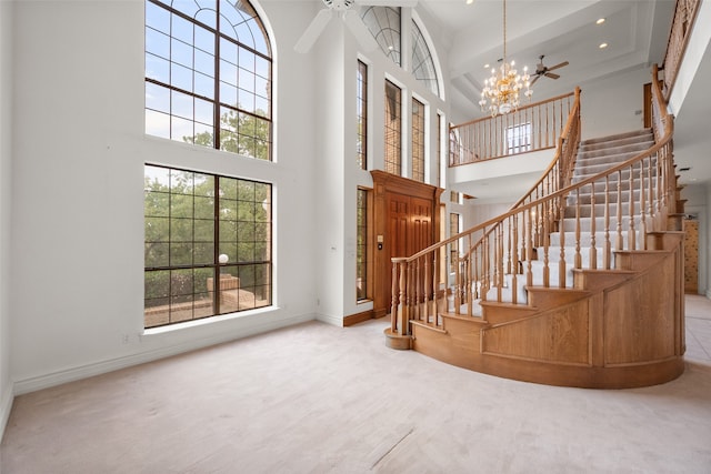 entryway featuring ceiling fan with notable chandelier, a wealth of natural light, a towering ceiling, and carpet floors