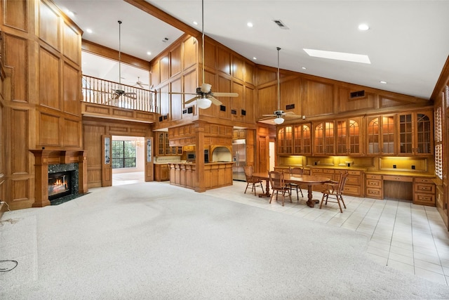 interior space featuring a high end fireplace, light carpet, wooden walls, ceiling fan, and high vaulted ceiling