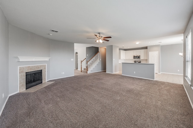 unfurnished living room with light colored carpet, a tile fireplace, and ceiling fan