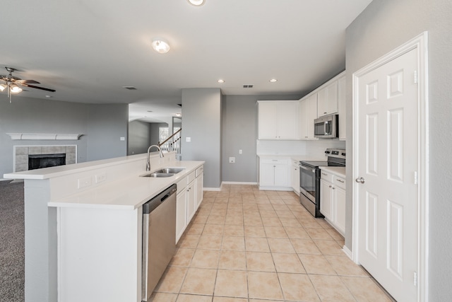 kitchen featuring sink, white cabinets, appliances with stainless steel finishes, a fireplace, and ceiling fan