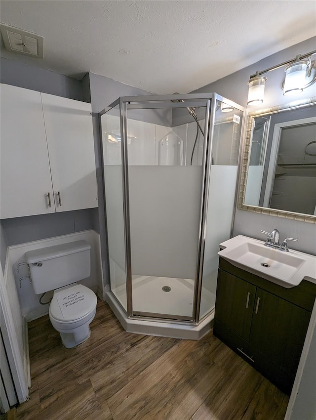 bathroom with a textured ceiling, wood-type flooring, toilet, a shower with shower door, and vanity