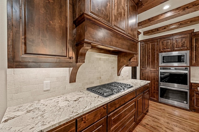 kitchen with light stone countertops, appliances with stainless steel finishes, light wood-type flooring, dark brown cabinets, and decorative backsplash