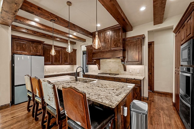 kitchen with stainless steel appliances, beamed ceiling, decorative light fixtures, dark wood-type flooring, and a kitchen island with sink