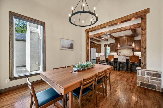 dining space featuring dark wood-type flooring, beamed ceiling, a wealth of natural light, and an inviting chandelier